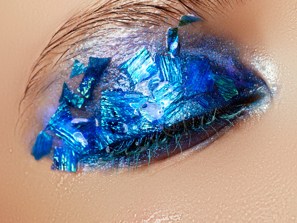 Cosmetics and make-up. Closeup macro shot of fashion sparcle visage. Closeup portrait of beautiful young woman with blue foil on face. Creative makeup - Foto, afbeelding