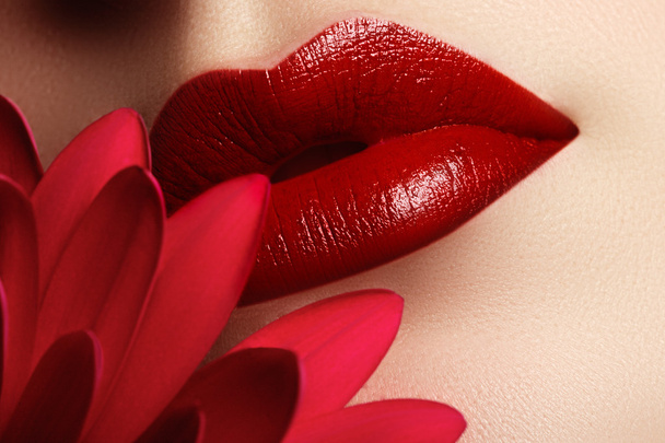 Gros plan belles lèvres féminines avec un maquillage rouge vif. Parfait peau propre, maquillage des lèvres sexy. Magnifique portrait spa avec fleur rouge tendre. Spa et cosmétiques
 - Photo, image
