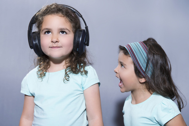 Smiling girl listening to music in headphones with sister scream - Foto, Bild