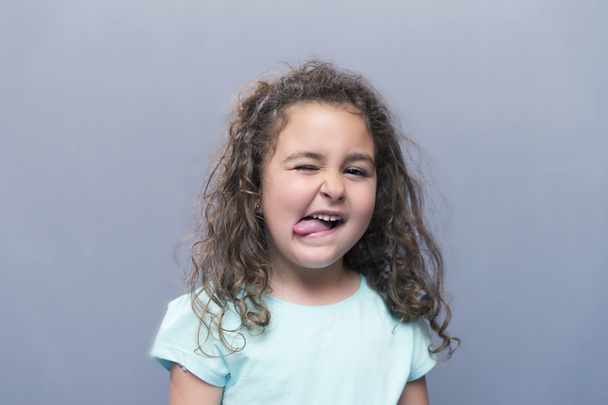 Little girl squinting eyes while showing tongue at camera - Foto, Imagen