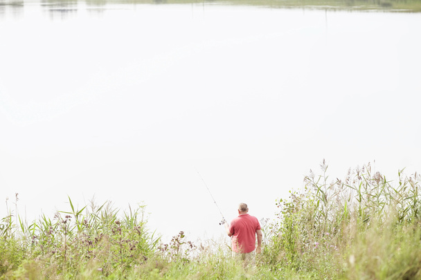Зрелый рыбак ловит рыбу на озере
 - Фото, изображение