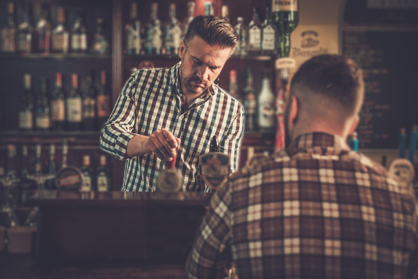 Przystojny barman nalewania piwa do klienta w pubie. - Zdjęcie, obraz