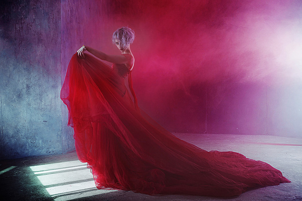 Fashion photo of young magnificent woman in red dress. Textured background, smoke - Foto, Imagem