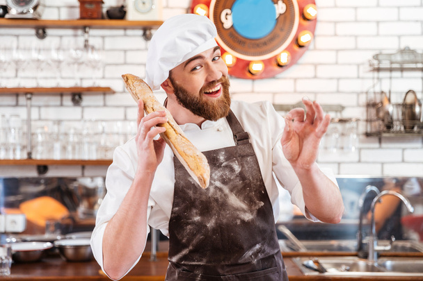 Happy baker holding loaf of bread and showing ok sign - Fotografie, Obrázek