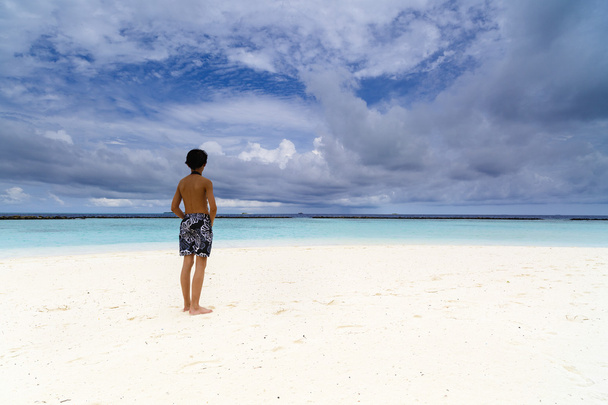 エキゾチックなビーチの上に座って、海を見た少年 - 写真・画像