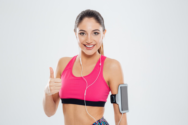 Smiling fitness woman with earphones showing thumb up - Foto, Imagem