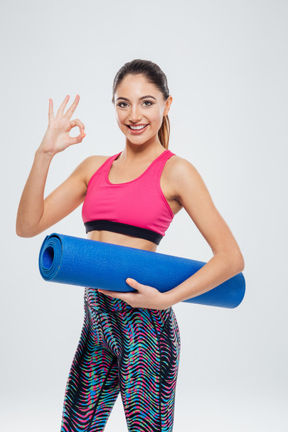 Woman holding yoga mat and showing ok sign with fingers - Foto, Imagem