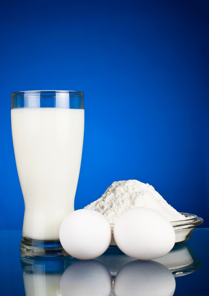 Fresh eggs, flour and milk on a dark blue background - Foto, afbeelding
