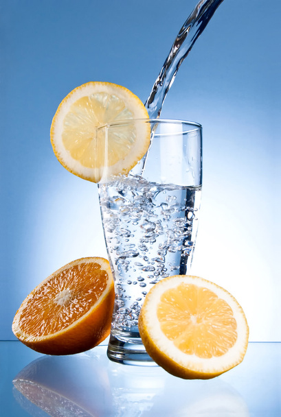 Vaso de agua mineral con limón y naranja sobre fondo azul
 - Foto, imagen