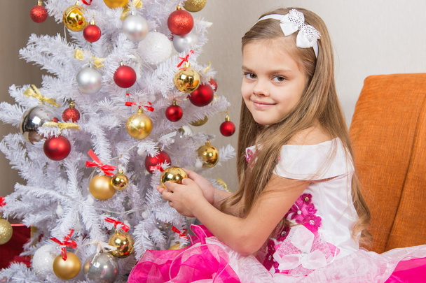 Семилетняя девочка в красивом платье угощает рождественскими игрушками и смотрит в рамку
 - Фото, изображение