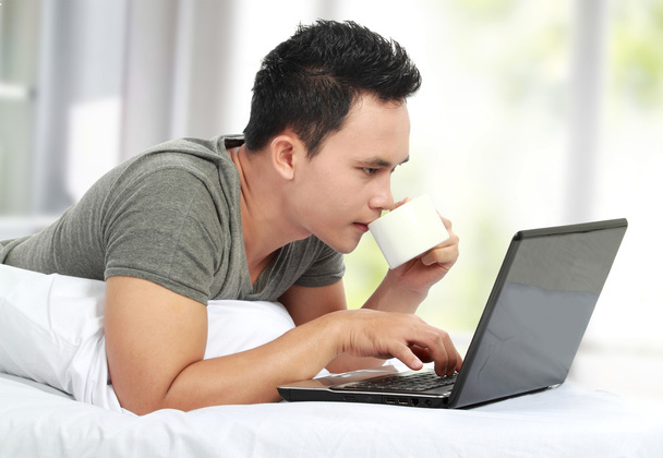 Man lying on a bed and using a laptop computer - Foto, Imagem