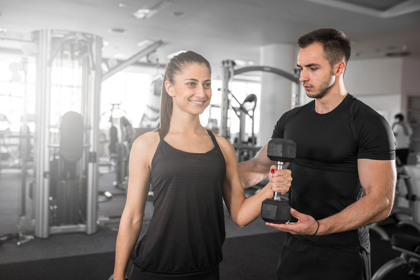Woman doing bicep curls in gym with her personal trainer - Foto, Bild