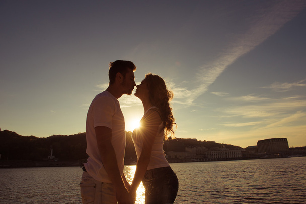Silhouette eines verliebten Paares, das sich küsst und den Sonnenuntergang beobachtet - Foto, Bild