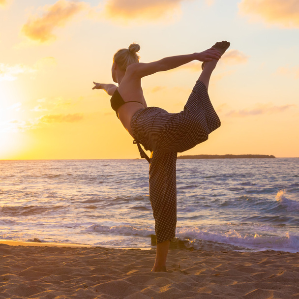 Женщина практикует йогу на морском пляже на закате. - Фото, изображение