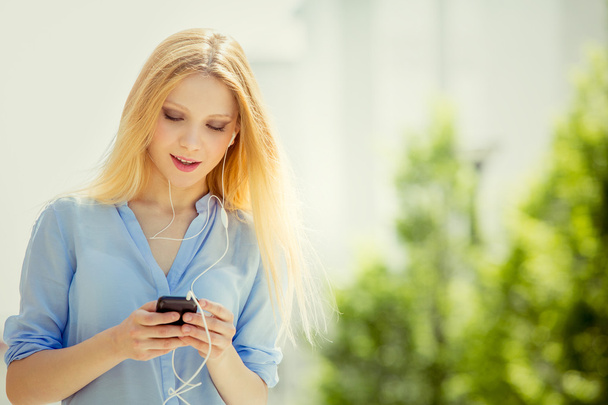 souriant blonde jeune femme texte avec téléphone se détendre dans un jardin
 - Photo, image