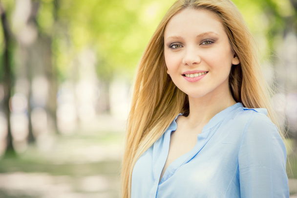 smiling blonde young woman portrait in a green cityscape - Photo, Image