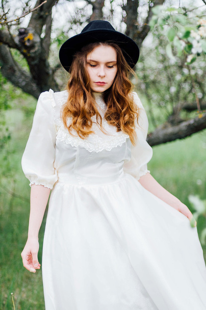 Jong meisje in een witte jurk en zwarte hoed in de in de witte fl - Foto, afbeelding