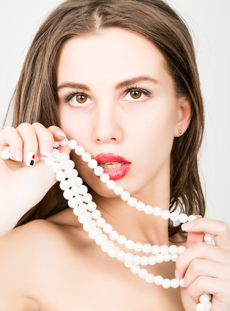 close-up portrait of a beautiful girl with red lips, holding a pearl necklace. mouth open, pearls touches her lips. Red Sexy Lips and Nails closeup - Foto, afbeelding
