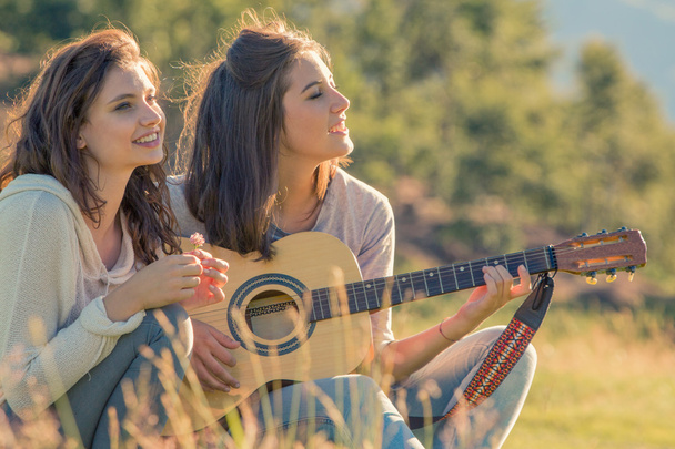 Young woman sing playing guitar with friend on sunset outdoor - Fotografie, Obrázek