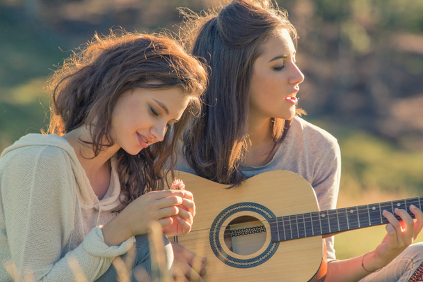 Young woman sing playing guitar with friend on sunset outdoor - Photo, image