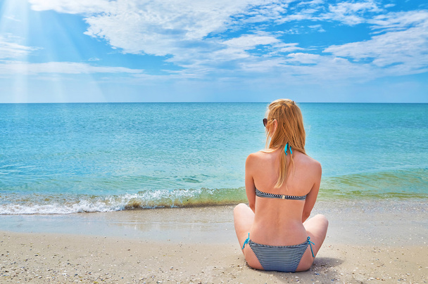 Молода жінка відпочиває біля моря, сидячи на піску
 - Фото, зображення
