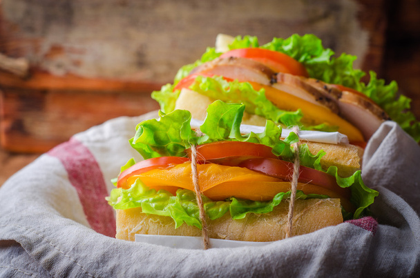 Домашний сэндвич со свежими помидорами и куриной грудкой в корзине на деревянном фоне. Выборочный фокус. Концепция пикника
 - Фото, изображение