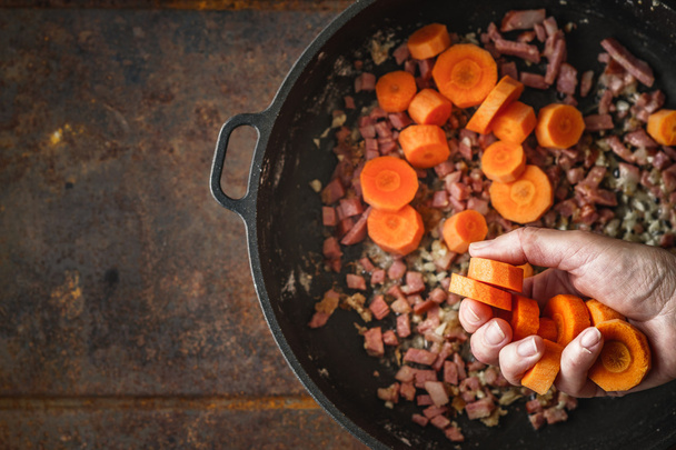 Adding carrots in the pan with bacon top view - Fotó, kép