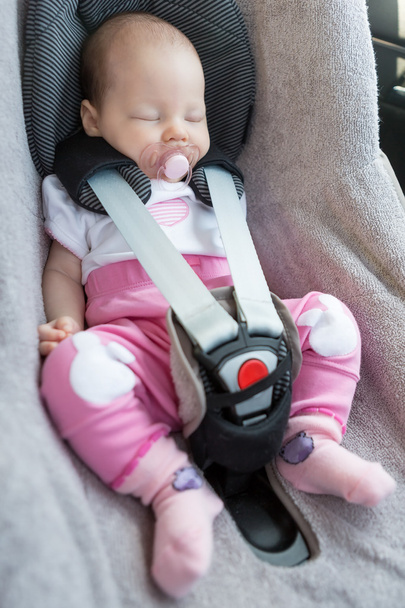 Новорожденная девочка сидит в автомобильном кресле с пристегнутым ремнем безопасности
 - Фото, изображение
