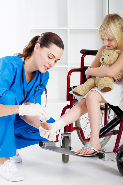 Caring nurse bandage little girl's ankle - Foto, imagen