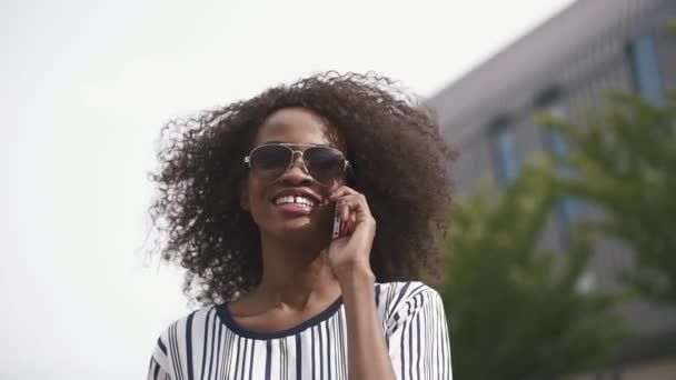 Beautiful happy african american business woman in sunglasses talking by the phone and smiling. Cityscape background - Felvétel, videó