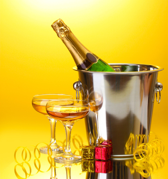 Champagne bottle in bucket with ice and glasses of champagne, on yellow background - Foto, Bild