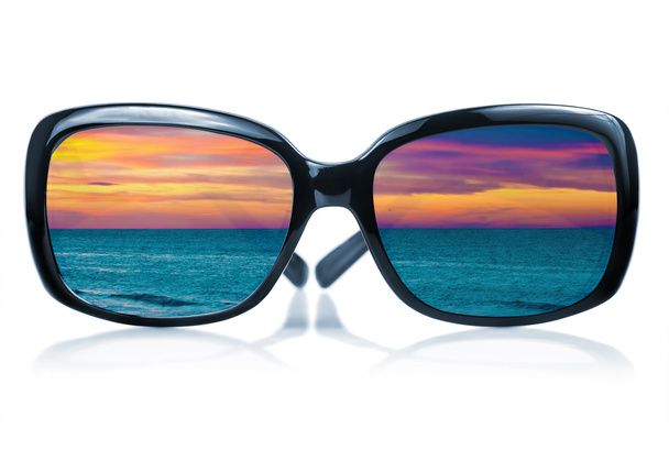 Sonnenbrille, die einen Sonnenuntergang am Meer widerspiegelt - Foto, Bild
