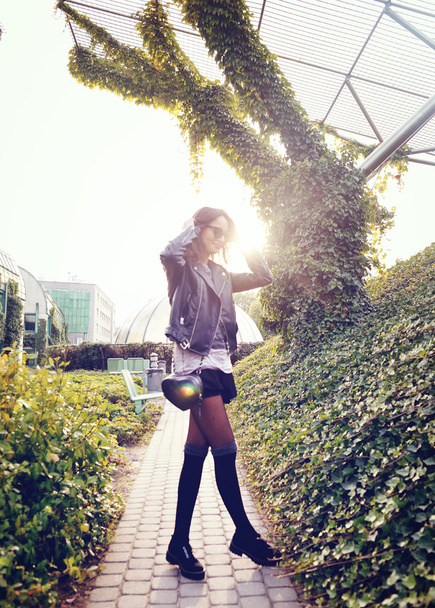 fashion model in sunglasses and black leather jacket posing outdoor - Fotoğraf, Görsel