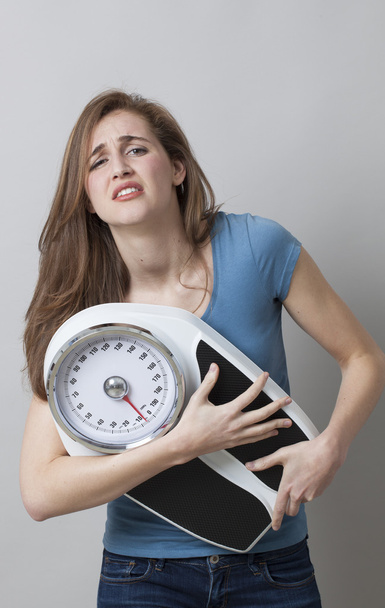 displeased young woman in pain with weighting scale in hands - 写真・画像