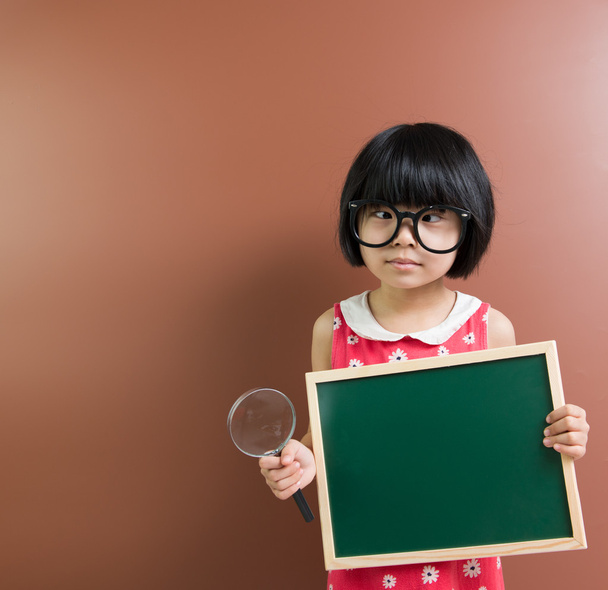 Παιδί της Ασίας σχολείο κρατήστε ένα μαυροπίνακα και Μεγεθυντικός φακός - Φωτογραφία, εικόνα