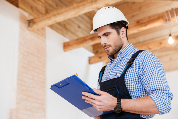 Happy builder writing notes in hardhat with clipboard - 写真・画像