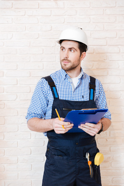 Builder thinking about something and holding a clipboard - Foto, Imagen