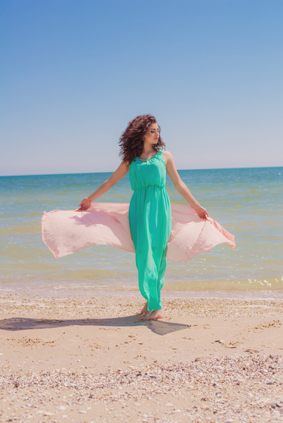 Young girl on the beach in summer in a beautiful dress with a flying scarf - Foto, Imagen