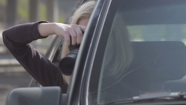 Blond girl watching and taking photos with professional camera in  car - Imágenes, Vídeo