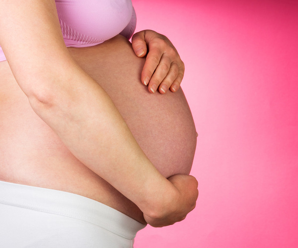 Pregnant woman with hands on her stomach, pink background. - Photo, Image