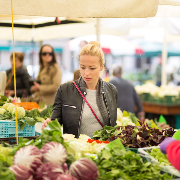 Женщина покупает овощи на местном продовольственном рынке
. - Фото, изображение