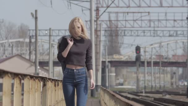 Young pretty shy model walking on the railway and smiling while windy - Séquence, vidéo
