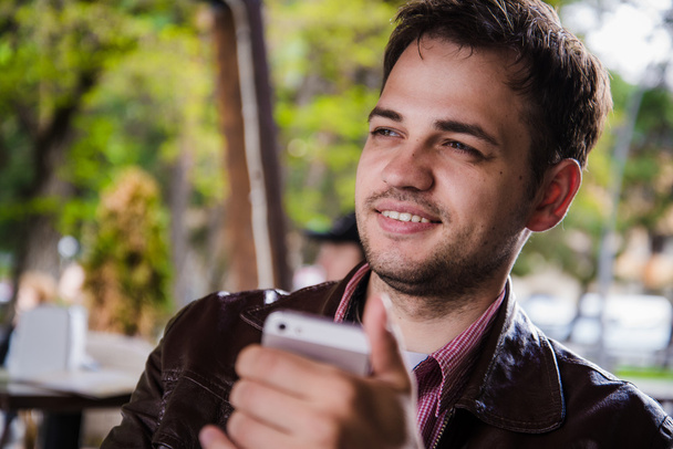 Smartphone hombre SMS mensajes de texto en la cafetería al aire libre en la terraza en verano. Feliz adulto joven urbano casual sosteniendo la lectura del teléfono o usando la aplicación para conectarse con amigos en las redes sociales
 - Foto, imagen