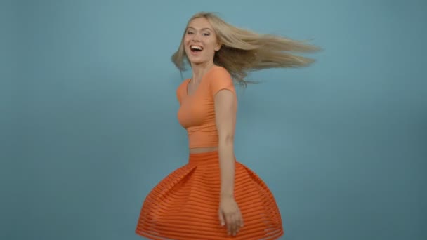 Szczęśliwa Młoda Blondynka modelu odwrotu pomarańczowy Top i Spódniczka na niebieskim tle - Materiał filmowy, wideo