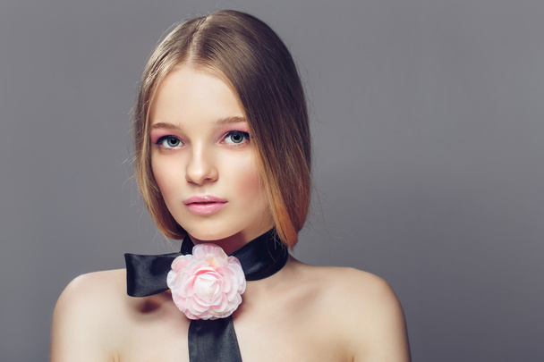 Portrait of young beautiful healthy woman with fancy pink rose on a strip over her neck. Gray background - Photo, image