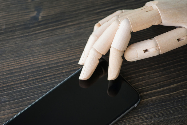 Artificial wooden hand with modern phone on wooden board - Φωτογραφία, εικόνα