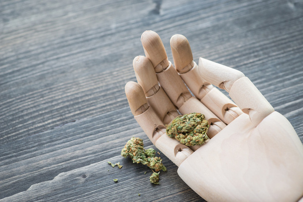 Artificial hand holding a weed over the rustic wooden board - Photo, Image