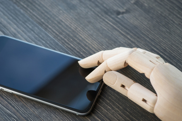 Artificial wooden hand with modern phone on wooden board - Φωτογραφία, εικόνα