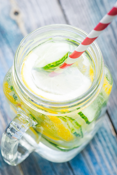 Jug with lemon and cucumber infused water on a rustic wooden surface - Photo, Image