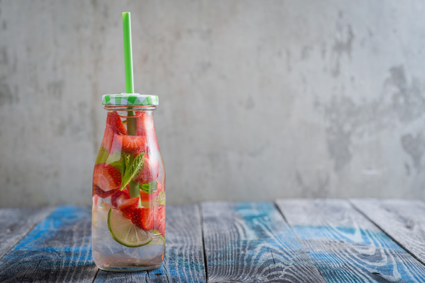 Bottle with lime and strawberry infused water on a rustic wooden surface - Fotó, kép